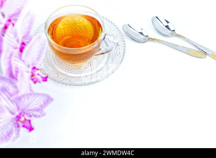 a transparent cup of aromatic tea and a pink orchid on a white background. Stock Photo