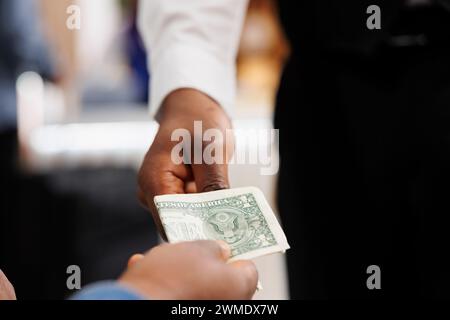 Close up of hospitality worker accepting of cash payment, taking money from customer. Hotel guest holding money paying for services at resort, giving tip to waiter at bar or restaurant Stock Photo
