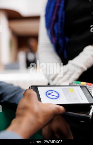 Male hotel guest making cashless payment using smartphone, phone and card reader machine, close up. Tourist paying for services with phone. Waiter accept contactless NFC payment from customer Stock Photo