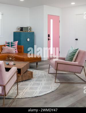 Trendy mid-century modern living room with pink chairs, a pink door, and leather sofa. Stock Photo