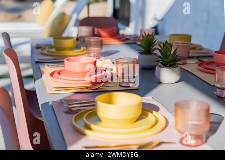 Set dining table outdoors with colorful bowls, plates, glasses, and silverware Stock Photo