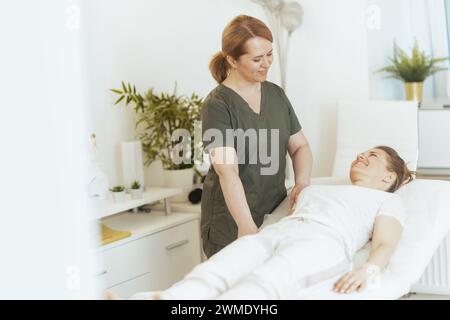 Healthcare time. smiling female medical massage therapist in massage cabinet with client doing checkup. Stock Photo