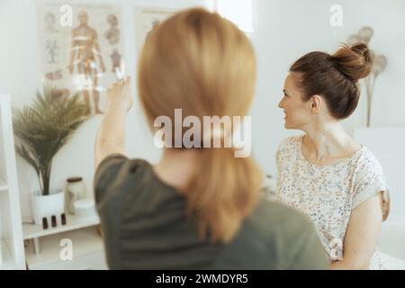 Healthcare time. Seen from behind female medical massage therapist in massage cabinet with client. Stock Photo