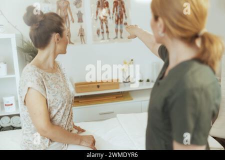 Healthcare time. Seen from behind female massage therapist in massage cabinet with client. Stock Photo