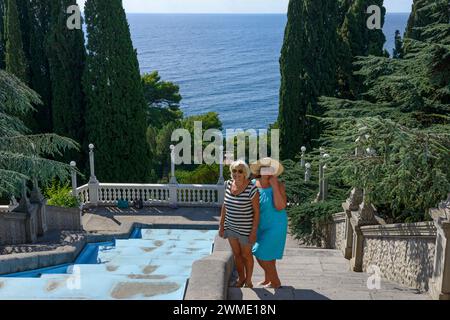 Two women are posing on stairway in decorative garden above the sea in Rodina sanatorium, Gaspra location, Crimea, Russia. Stock Photo