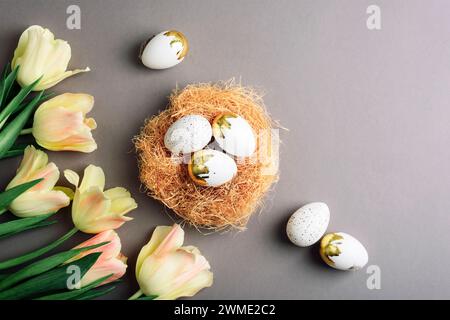 Easter nest with eggs and light yellow tulips on gray background. Top view, flat lay, copy space. Stock Photo