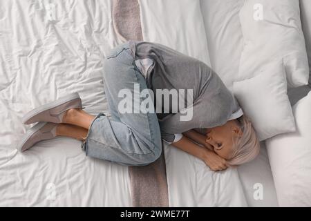 Depressed mature woman lying on bed, top view Stock Photo