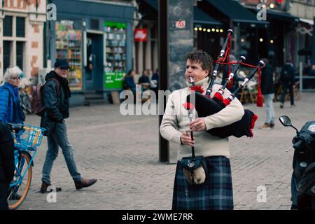 Gent, Belgium - January 31 2024: iper in traditional Scottish outfit plays on bagpipes in city of gent with people and tourist watching it Stock Photo