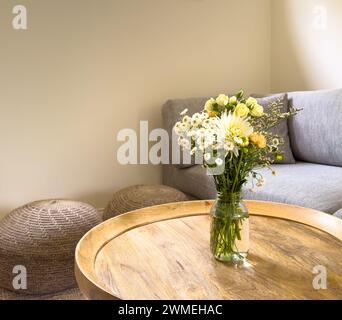 Fresh cut flowers in a jar on a round wooden coffee table in a lounge room Stock Photo