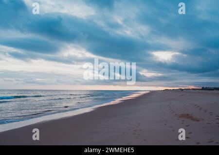 Evening sky, adorned with dramatic clouds, looms over a deserted beach with a glowing horizon Stock Photo