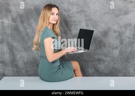 Attractive young lady with blond hair using a laptop while sitting on a table Stock Photo