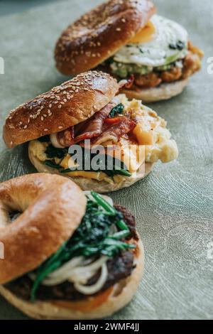 Top-down view of three breakfast sandwiches stacked toasted bagels with sesame seeds and filled with eggs, spinach, and cheese Stock Photo