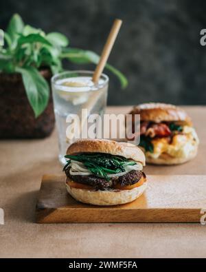 A close-up of a sandwich on a cutting board with bread, lettuce, tomato, cheese, and glass drink on wooden plate Stock Photo