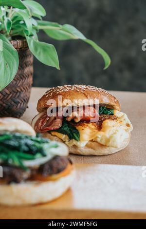 A breakfast bagel sandwich with scrambled eggs, spinach, and cheese on a plate Stock Photo