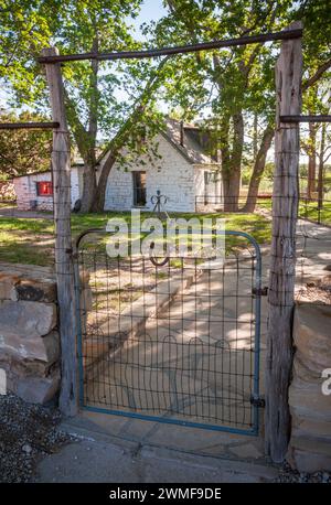 A wire gate between wooden posts leads along a flagstone path to a whitewashed building at Frijole Ranch, Guadalupe Mountains National Park, Texas. Stock Photo