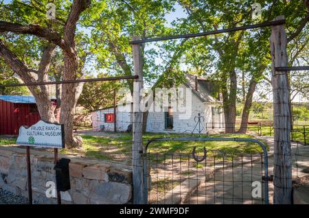 A wire gate between wooden posts opens toward a whitewashed stone building under trees at Frijole Ranch, Guadalupe Mountains National Park, Texas. Stock Photo