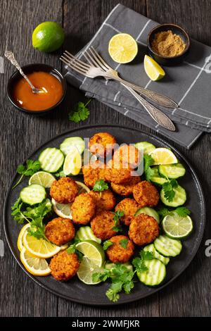 fried rice cakes, rice tikki, indian style on black plate served with cucumber, lemon, lime slices and sweet chili sauce on dark wooden table, vertica Stock Photo
