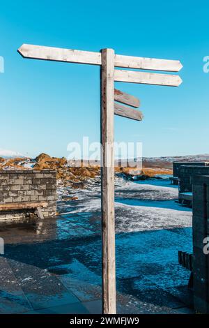 Wooden blank signboards placed on top of pole near concrete wall and shabby floor construction against flowing water and blue sky in daylight Stock Photo