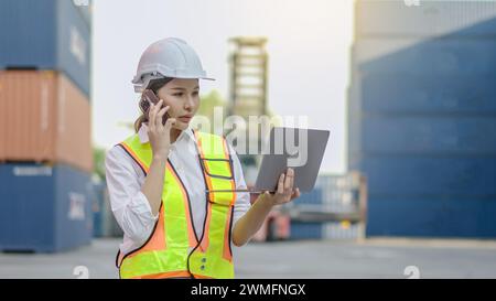 A female worker in protective gear holding a laptop talking on a smartphone Stock Photo
