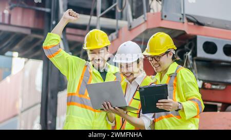 The cheerful dock workers with the supervisor, recording data online using a laptop at a warehouse Stock Photo