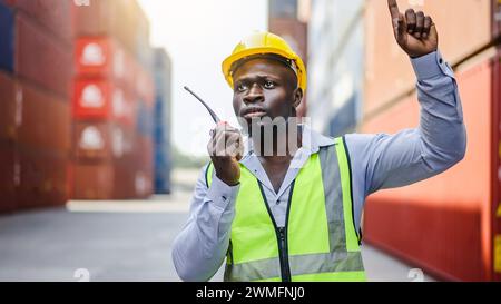 A dock foreman with a radio standing in front of cargo containers Stock Photo