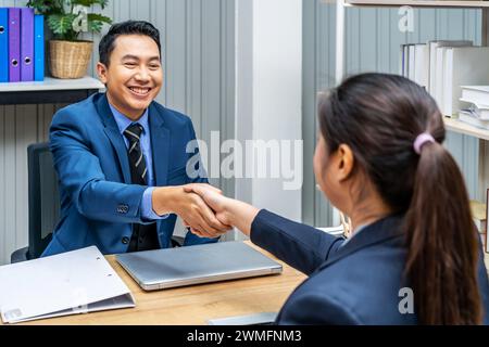 A young woman and man shake hands at a desk in agreement Stock Photo