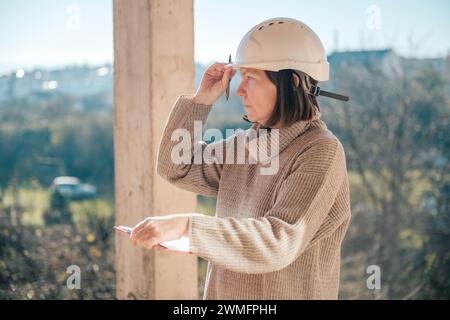 Female architect making notes and remarks during building site inspection, selective focus Stock Photo
