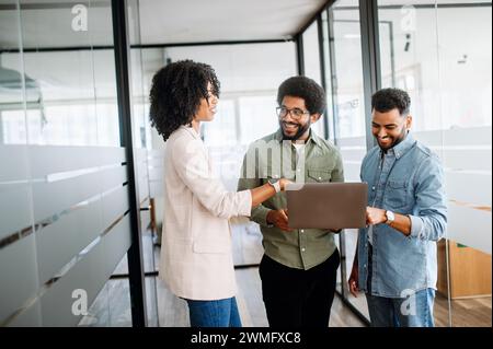 In a dynamic office setting, a businesswoman discusses on-the-go with two male colleagues, showcasing a versatile and agile work environment where teamwork and mobility are paramount Stock Photo