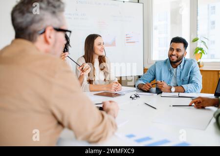 A diverse team sits at a table, engaging in a lively discussion with expressions of agreement and interest, epitomizing a productive brainstorming session in a bright, modern office setting Stock Photo