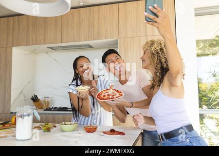 Young Asian man and two young biracial women enjoy making pizza at home Stock Photo