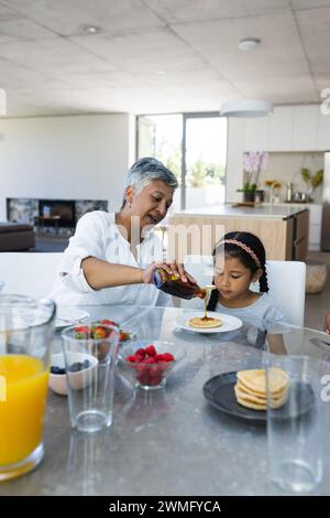 Biracial grandmother serves breakfast of pancakes to a biracial granddaughter at home Stock Photo
