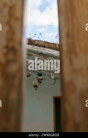 An old ceiling light in an abandoned building seen through wooden door Stock Photo