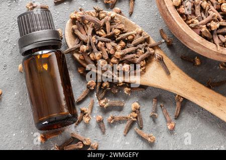 Close up glass bottle of essential clove oil and cloves in wooden spoon on rustic background. Herbs and spice oil concept Stock Photo