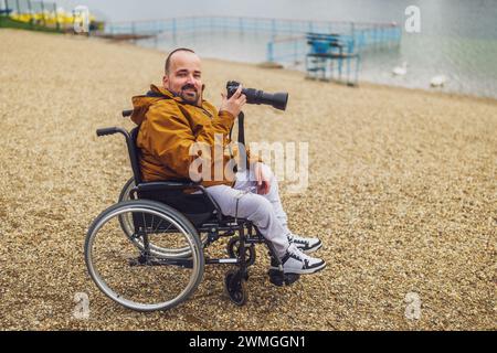 Paraplegic handicapped man in wheelchair is photographing outdoor. Stock Photo