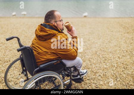 Paraplegic handicapped man in wheelchair is enjoying outdoor and drinking coffee. Stock Photo