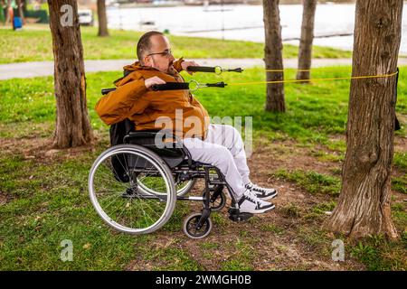 Paraplegic handicapped man in wheelchair is exercising with stretch band in park. Stock Photo