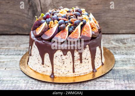 Delicious cake with figs dipped into melted chocolate, pecan nuts, grapes, chocolate bites and cookies on the top on rustic background Stock Photo