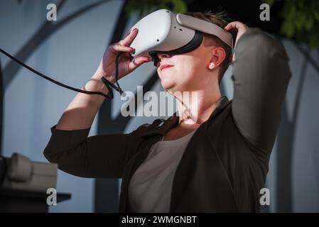 Smiling and delighted young woman enjoying VR experience, using virtual reality glasses in the natural history museum playroom. Stock Photo