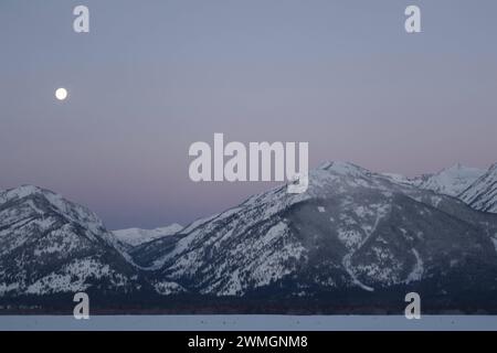 Monduntergang... Rocky Mountains  Wyoming, USA , Vollmond in eisklater Nacht über der Grand Teton Range vor zart rosa farbenem Nachthimmel, idyllische Winterstimmung, Landschaftsbild Vereinigte Staaten *** Daybreak with moonset above the Teton Range, purple sky over snow covered mountains, hills, close to Jackson Hole, Wyoming, USA Wyoming Nordamerika, Vereinigte Staaten von Amerika Stock Photo