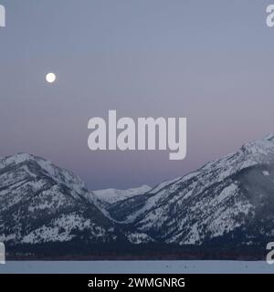 Monduntergang... Rocky Mountains  Wyoming, USA , Vollmond in eisklater Nacht über der Grand Teton Range vor zart rosa farbenem Nachthimmel, idyllische Winterstimmung, Landschaftsbild Vereinigte Staaten *** Daybreak with moonset above the Teton Range, purple sky over snow covered mountains, hills, close to Jackson Hole, Wyoming, USA Wyoming Nordamerika, Vereinigte Staaten von Amerika Stock Photo