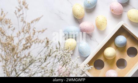 Colorful Easter eggs with golden spots in a wooden box on a white marble background and some flowers. Stock Photo