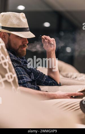 Portrait of a man smoking an electronic cigarette in the living room while looking at his cell phone Stock Photo