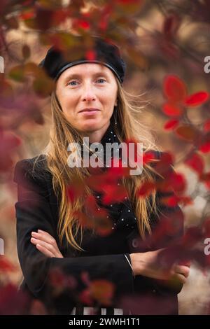 Chic Happy Young adult woman in a beret smiling framed and against a background of autumn greenery Stock Photo