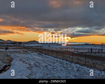 Sun setting over desert landscape with road and fence in foreground Stock Photo
