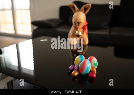 Group of easter eggs in different sizes and colors on table with blurry easter bunny in the background. Stock Photo