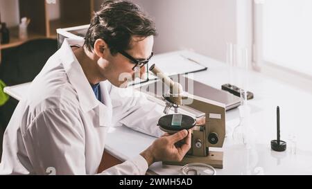 An adult male Caucasian scientist in glasses and a white coat works with a sample under study on a microscope. Color correction. Stock Photo