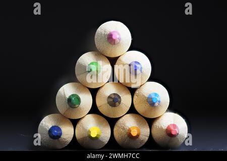 Ten colouring pencils placed on top of each other to form a triangle shape and showing just the tips of the sharpened pencils with a black background Stock Photo
