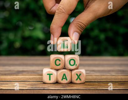 Carbon tax. Smoke factory icon in hand, put on top of wood cube blocks pyramid stack with green text, CO2 TAX on wooden desk. Environmental, social re Stock Photo