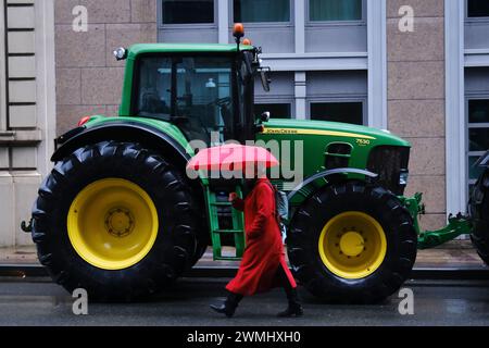 Brussels, Belgium. 26th Feb, 2024. Pedestrian walks in front of tractors during a protest of farmers over price pressures, taxes and green regulation in Brussels, Belgium on Feb. 26, 2024. Credit: ALEXANDROS MICHAILIDIS/Alamy Live News Stock Photo