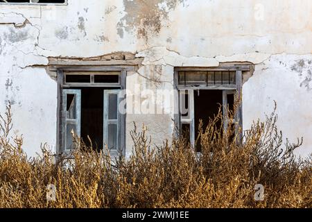 Neglected building facade with broken windows and blue window shutters in Al Jazirah Al Hamra haunted town in Ras Al Khaimah, United Arab Emirates. Stock Photo